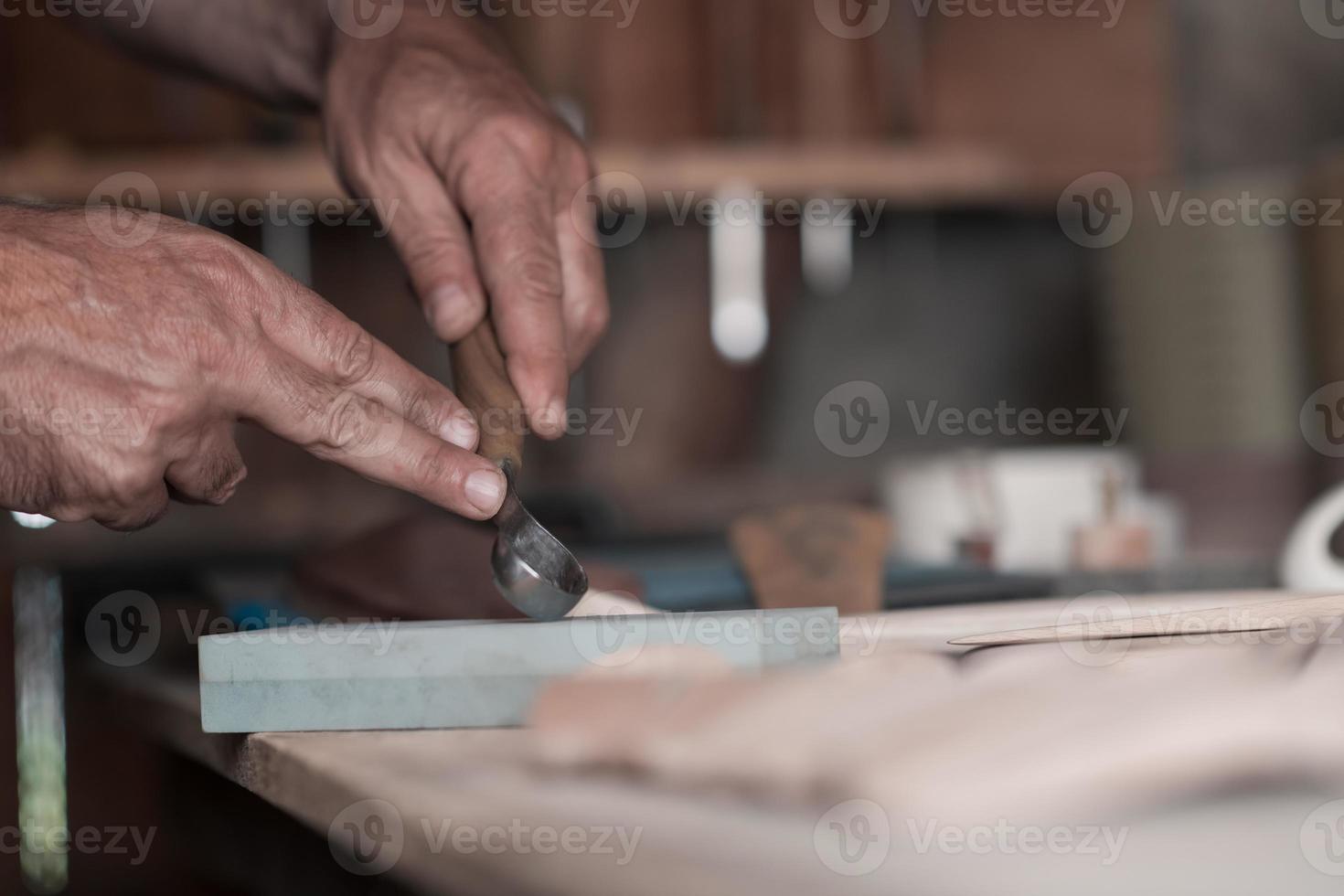 Hands carving spoon from wood, working with chisel close up. Wooden workshop. Process of making wooden spoon photo