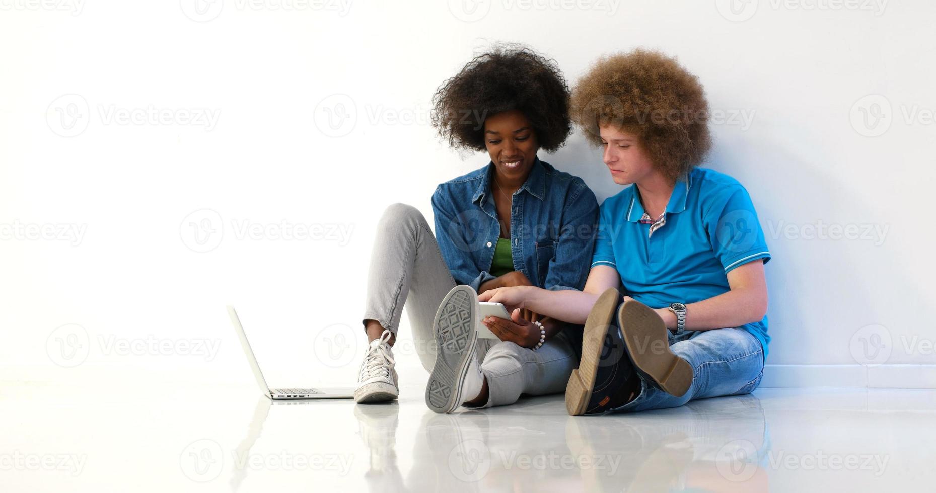 multiethnic couple sitting on the floor using a laptop and tablet photo