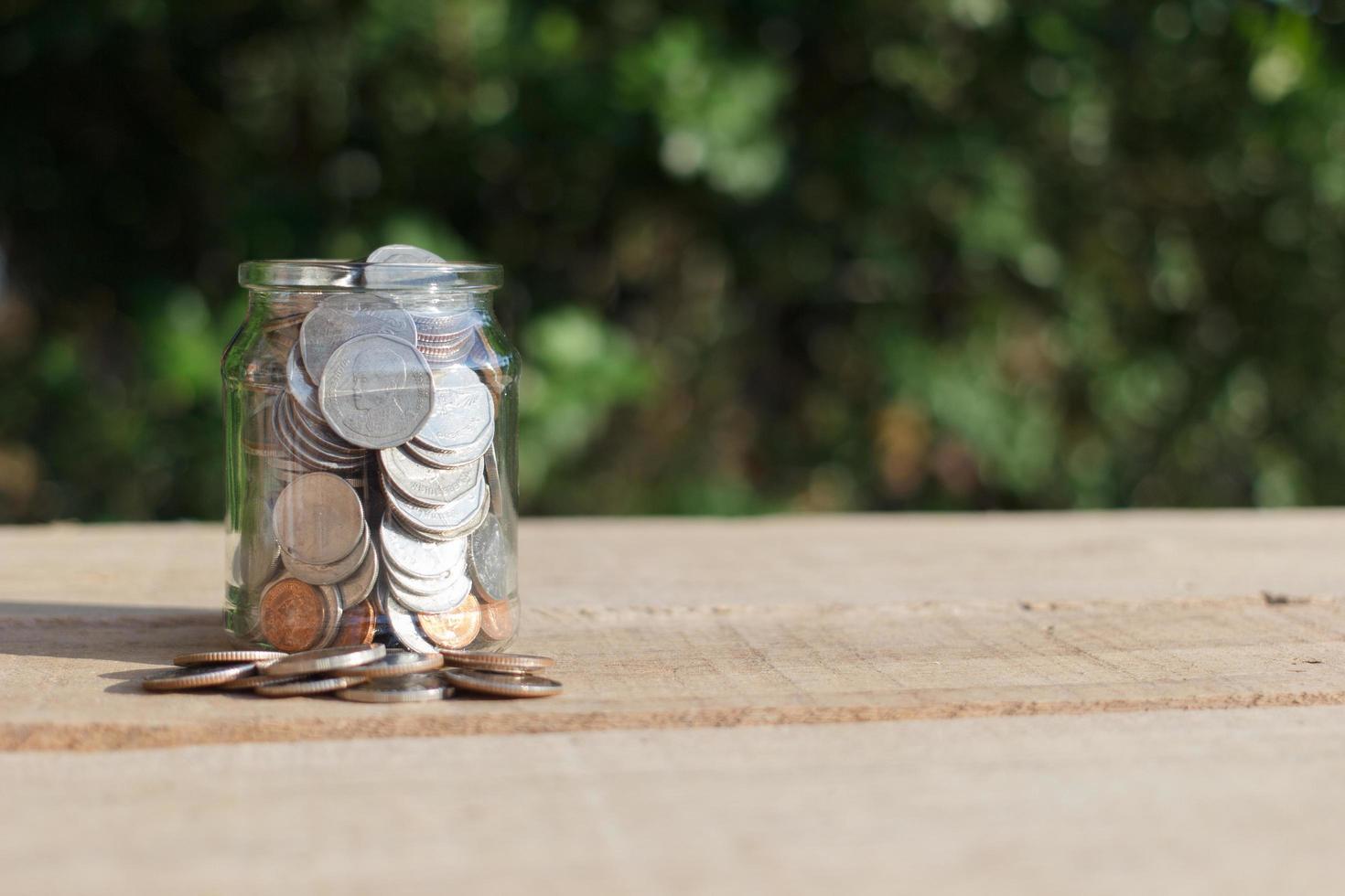 Coins in clear jar placed on wooden planks outdoors in the garden, investment saving concept.copy space. photo