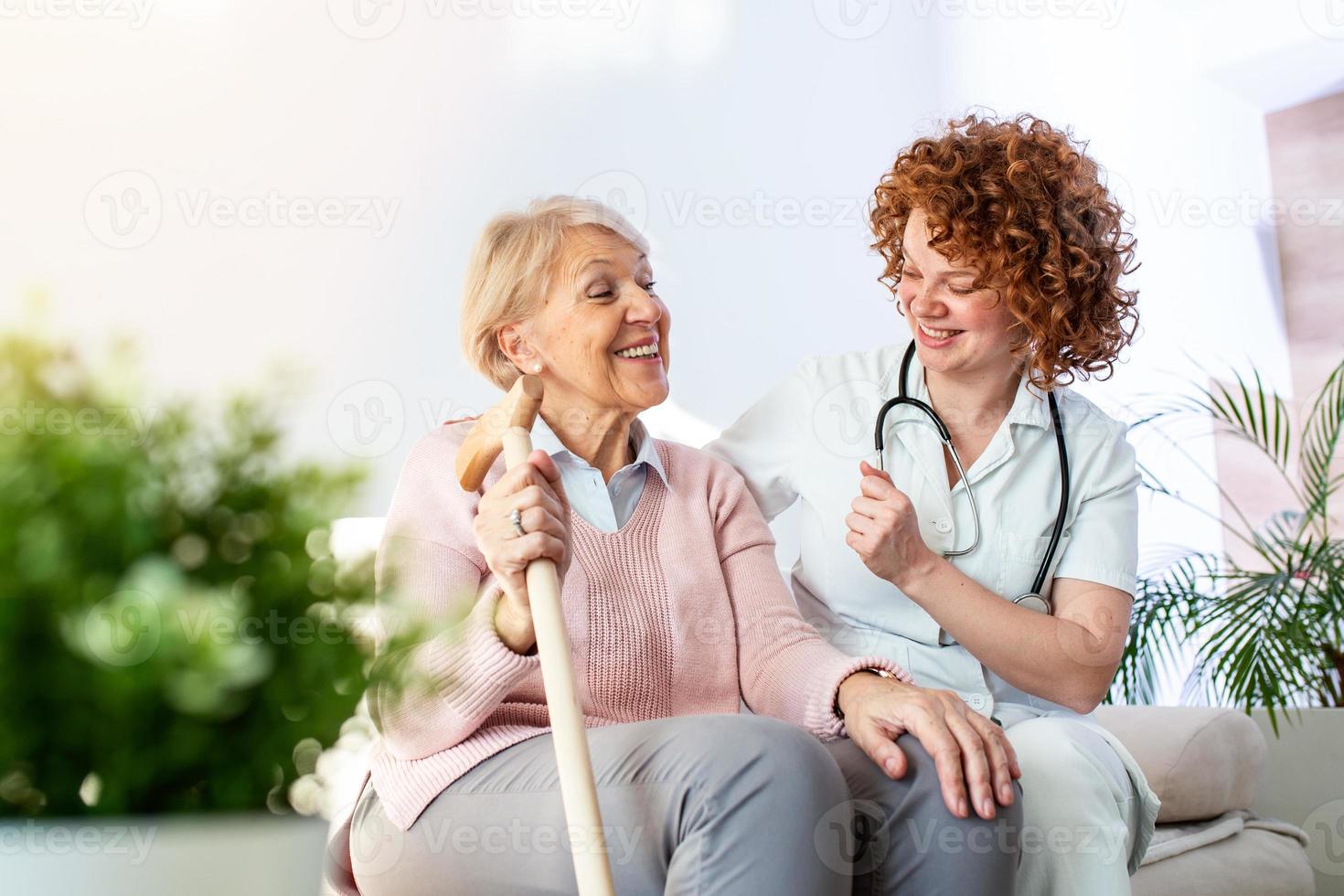 Friendly relationship between smiling caregiver in uniform and happy elderly woman. Supportive young nurse looking at senior woman. Young caring lovely caregiver and happy ward photo