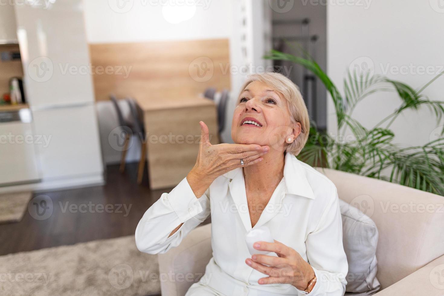 Beautiful mature woman holding jar of skin cream for face isolated on light blue background. Happy senior woman applying anti-aging moisturizer. Beauty and anti aging treatment. photo