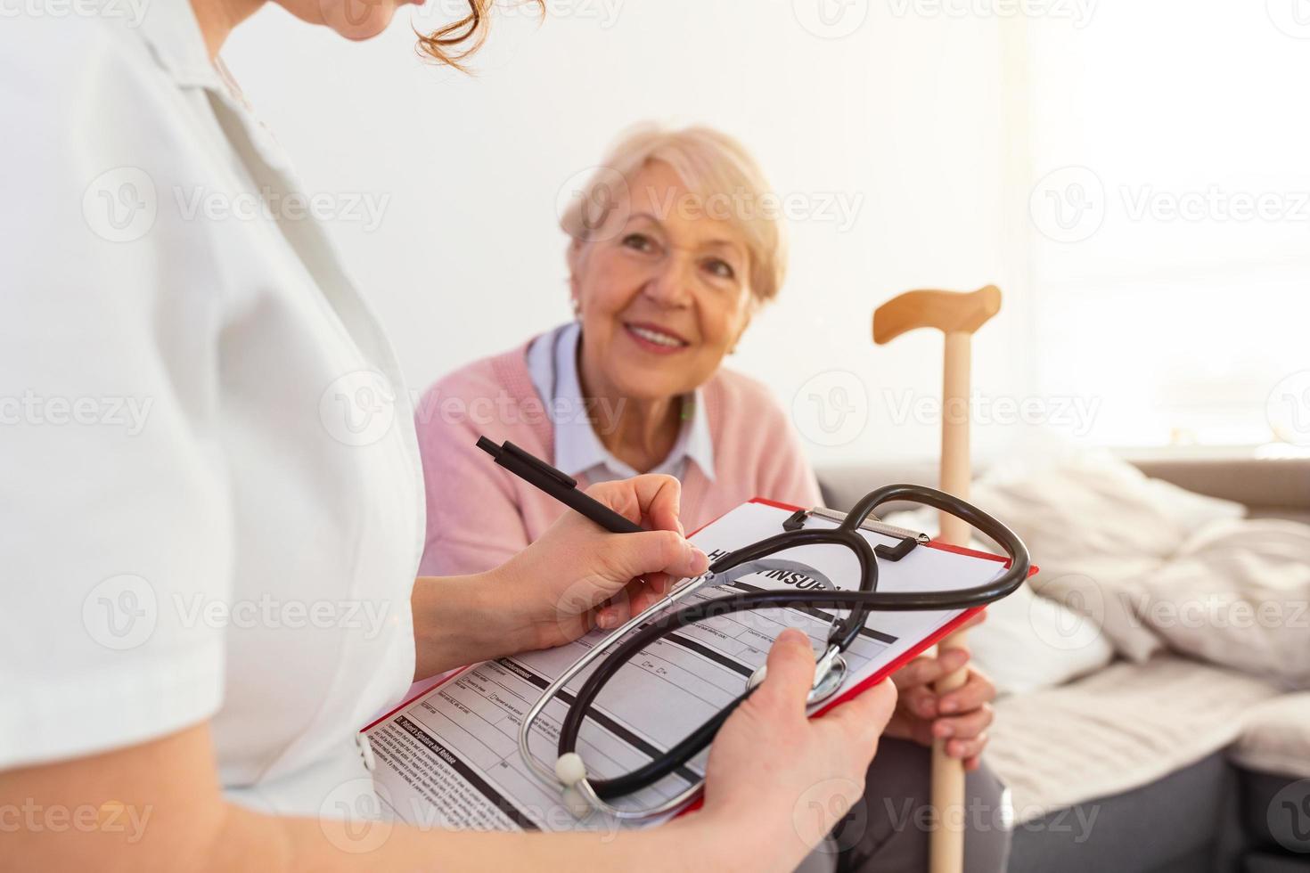 Senior woman is visited by her doctor or caregiver. Female doctor or nurse talking with senior patient. Medicine, age, health care and home care concept. Senior woman with her caregiver at home photo