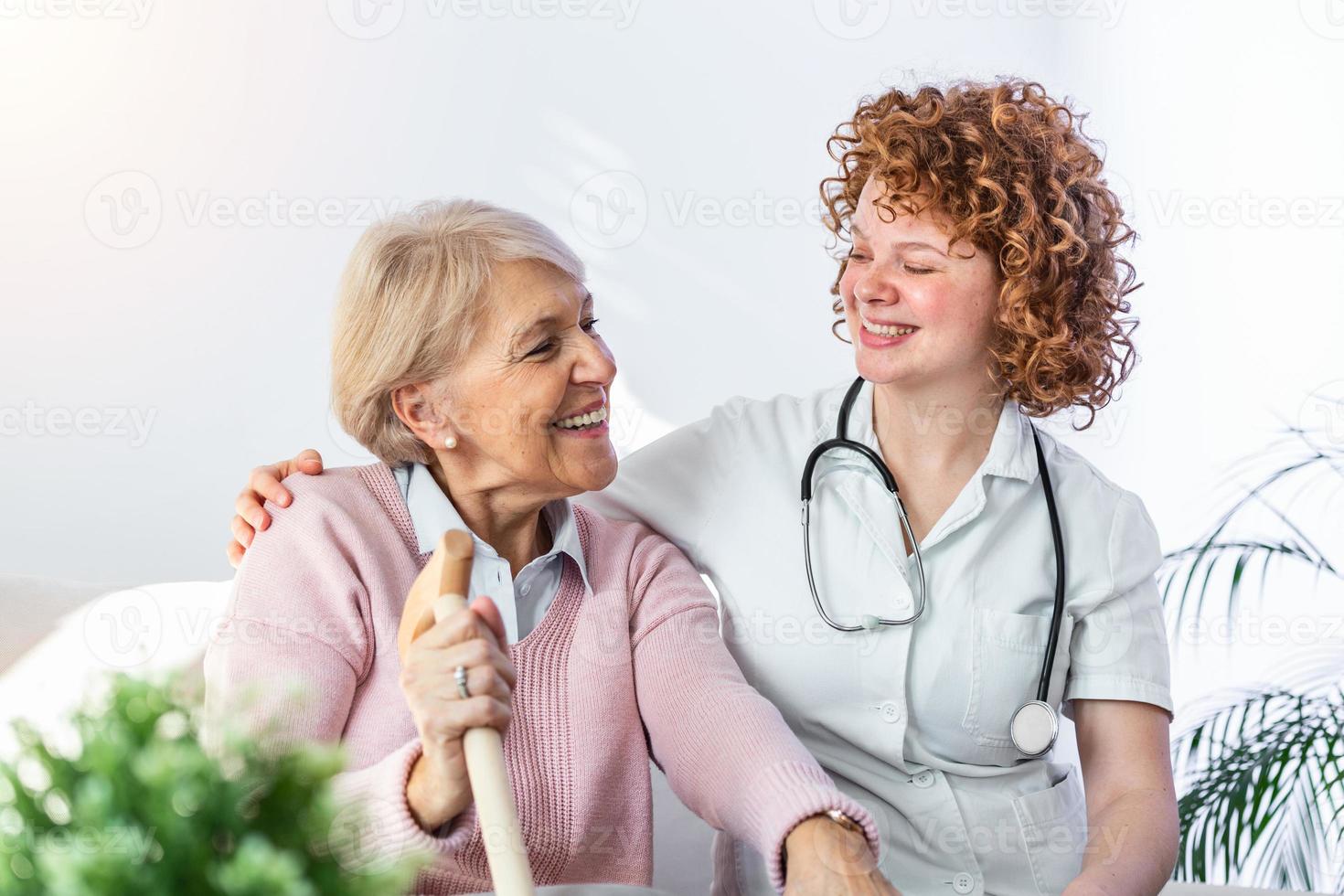 Friendly relationship between smiling caregiver in uniform and happy elderly woman. Supportive young nurse looking at senior woman. Young caring lovely caregiver and happy ward photo