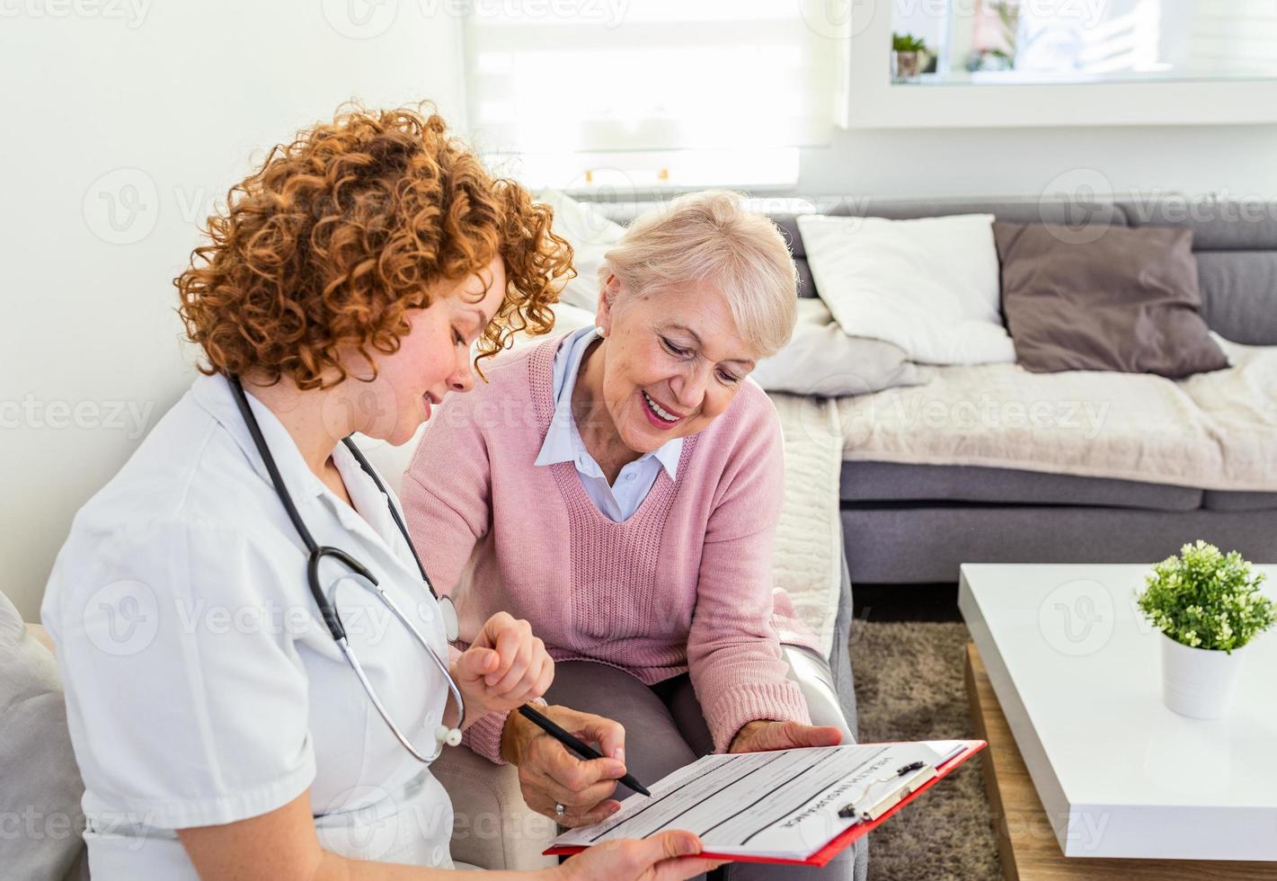 Senior woman is visited by her doctor or caregiver. Female doctor or nurse talking with senior patient. Medicine, age, health care and home care concept. Senior woman with her caregiver at home photo