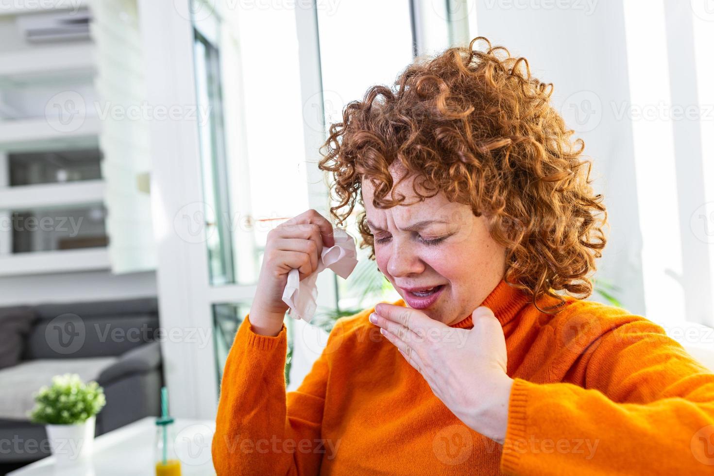 Sick desperate woman has flu. Rhinitis, cold, sickness, allergy concept. Pretty sick woman has runnning nose, rubs nose with handkerchief. Sneezing female. Brunette sneezing in a tissue photo