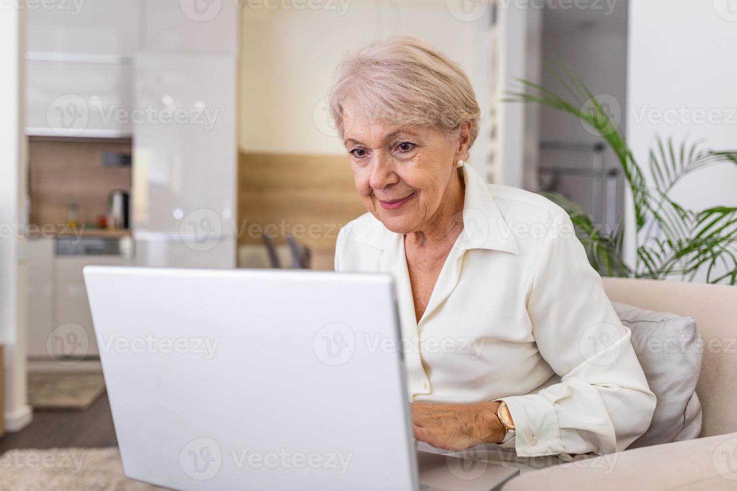 Elderly lady working with laptop. Portrait of beautiful older woman working laptop computer indoors. Senior woman using laptop at home, laughing photo