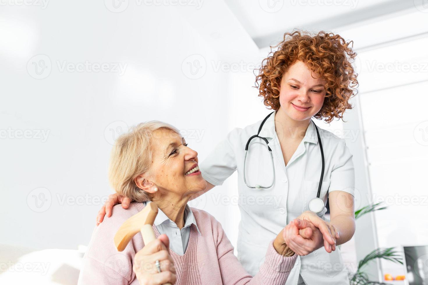Happy patient is holding caregiver for a hand while spending time together. Elderly woman in nursing home and nurse. Aged elegant woman at nursing home photo