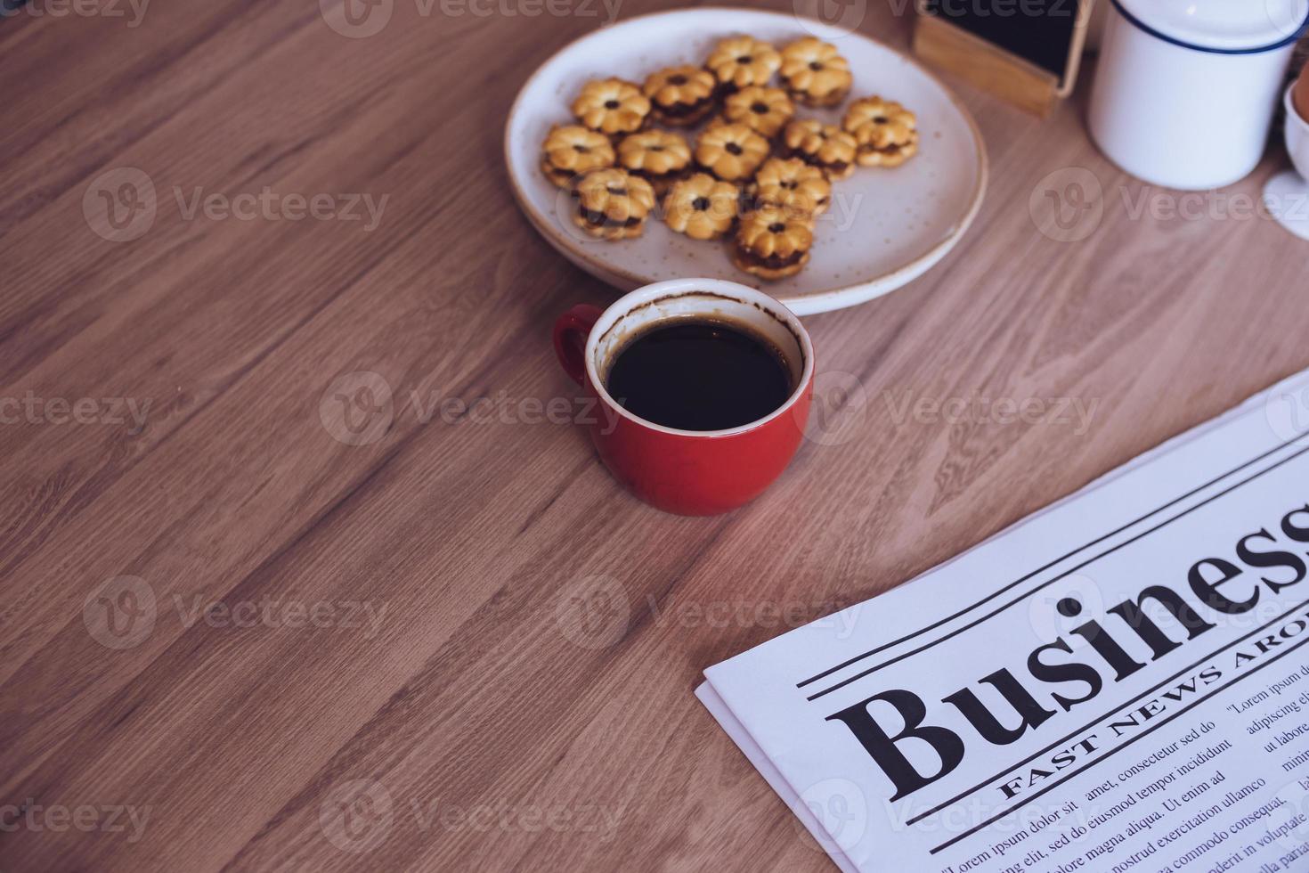 newspaper, a cup of coffee and snacks on a wooden table. photo