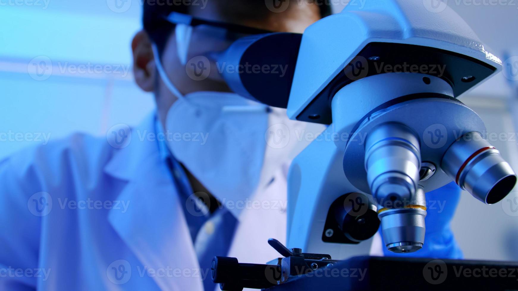 científico asiático investigando y mirando a través de un microscopio en laboratorio. foto