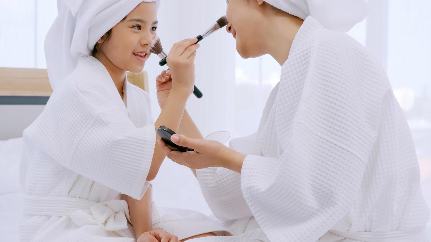 madre con hija pequeña en albornoces haciendo tratamiento de belleza juntos en el dormitorio. foto