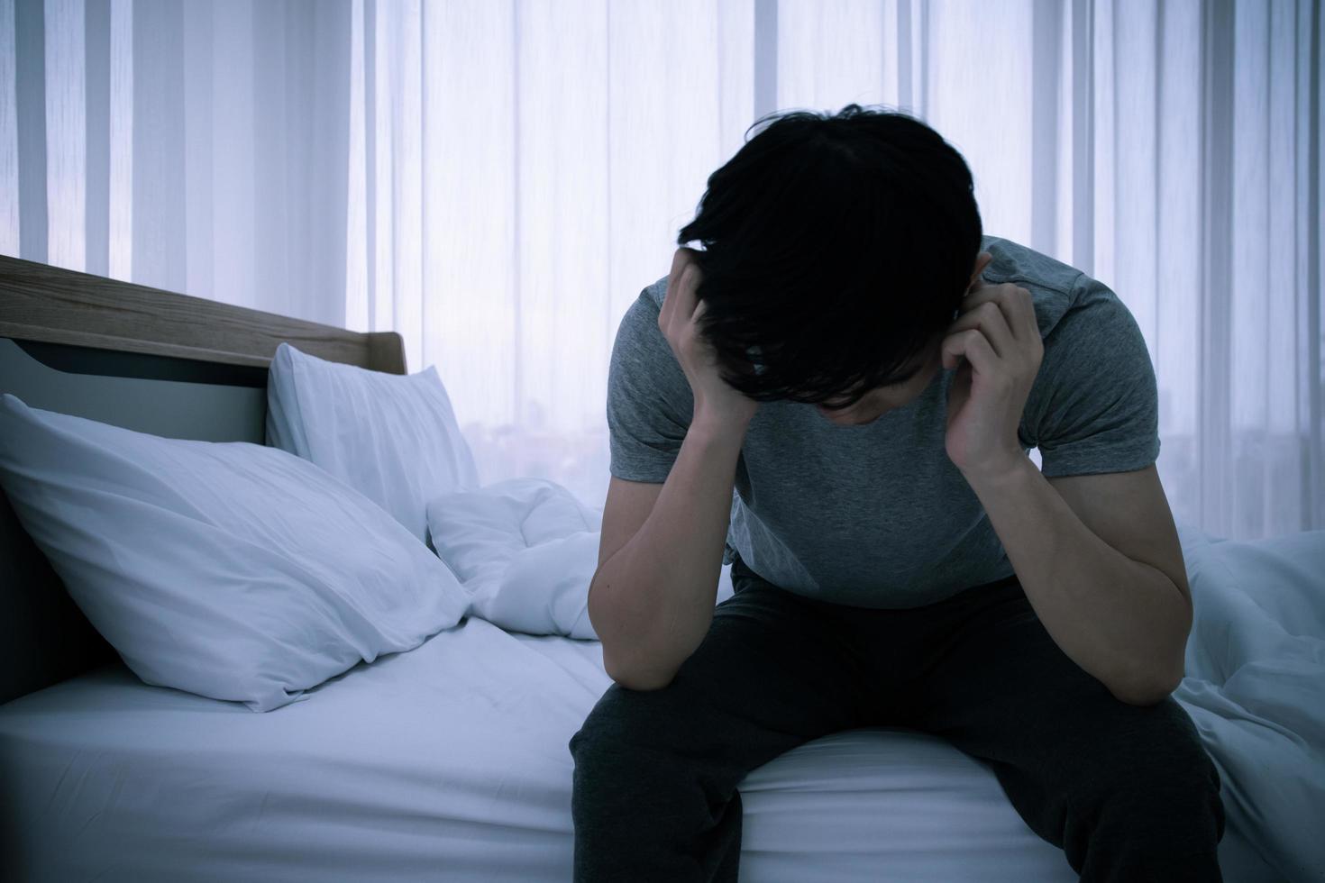 Un joven asiático estresado sentado solo en la cama. mala relación o problema en quiebra y concepto de enfermedad. foto