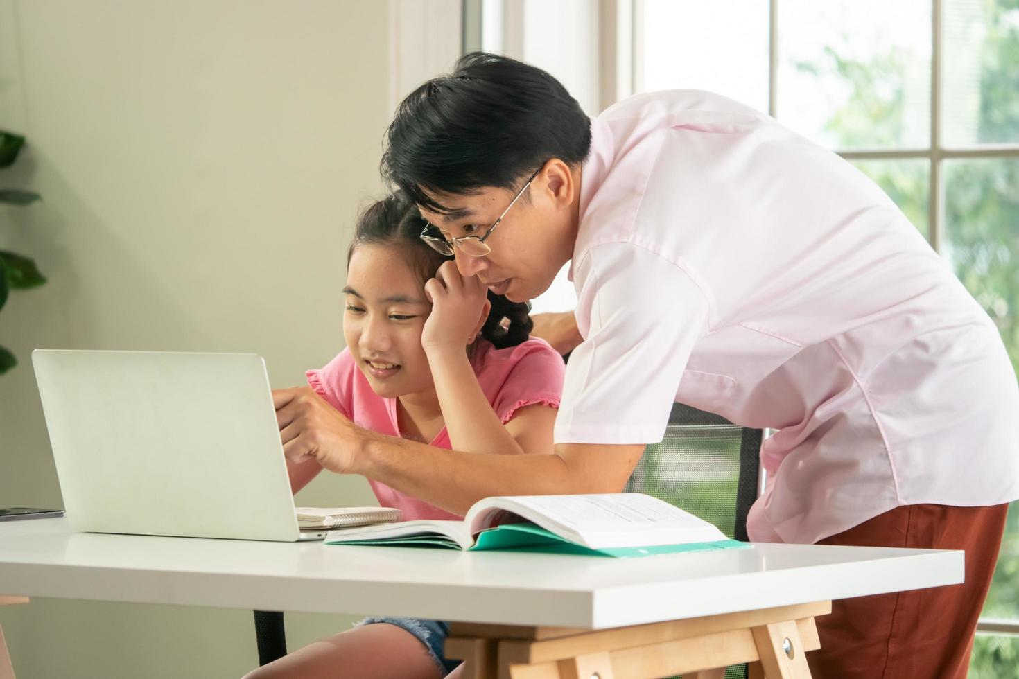 Father is teaching his daughter to do homework during online distance learning at home. photo