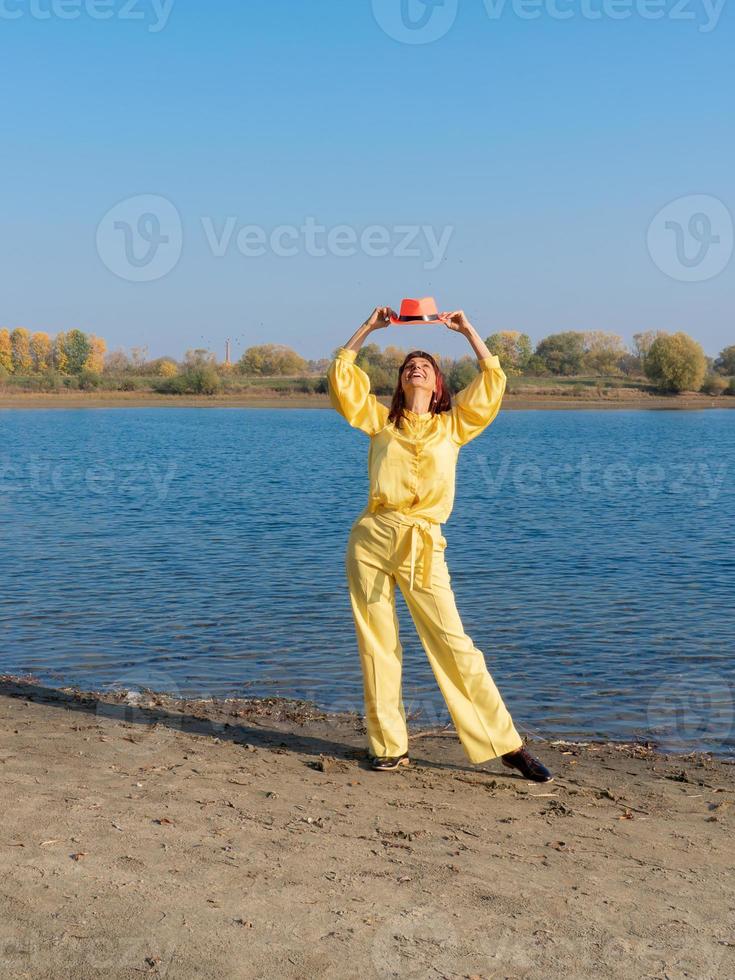 mujer vestida de amarillo con sombrero rojo posando junto al lago en otoño foto