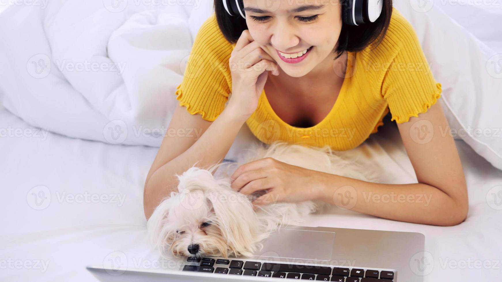Asian woman using a laptop computer and lying on a bed with shihtzu dog photo
