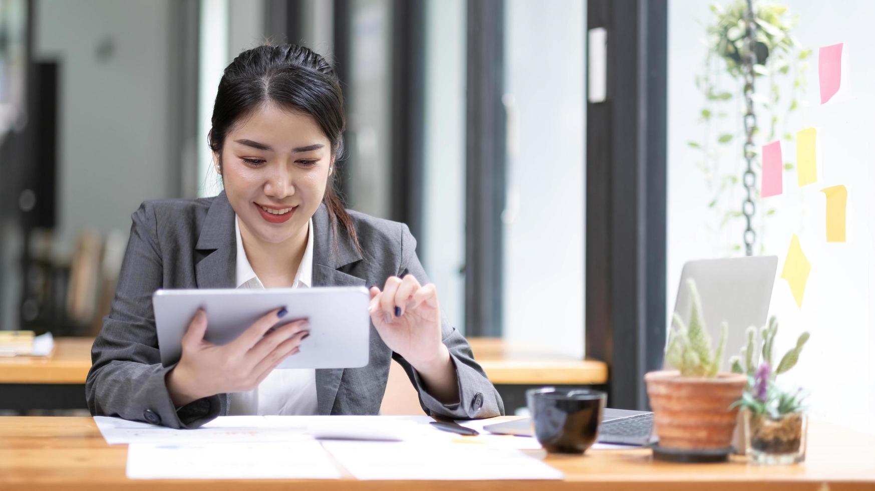 Beautiful smiling Asian businesswoman wearing glasses hand holding pen working using tablet at office. photo