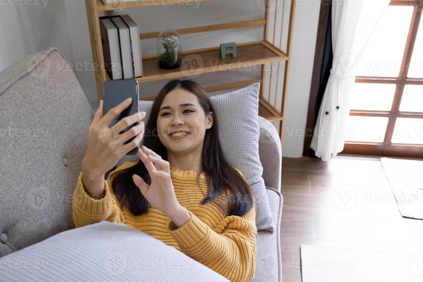 Young asian woman is using smartphone lie down on the sofa. Relax, happy, technology concept photo