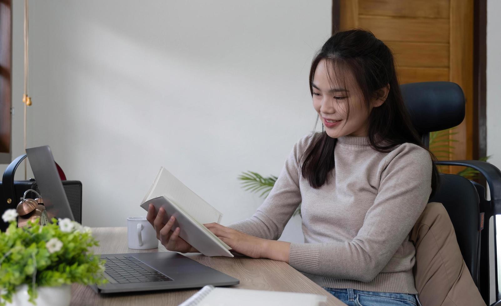Smiling Asian woman reading book while sitting at home photo