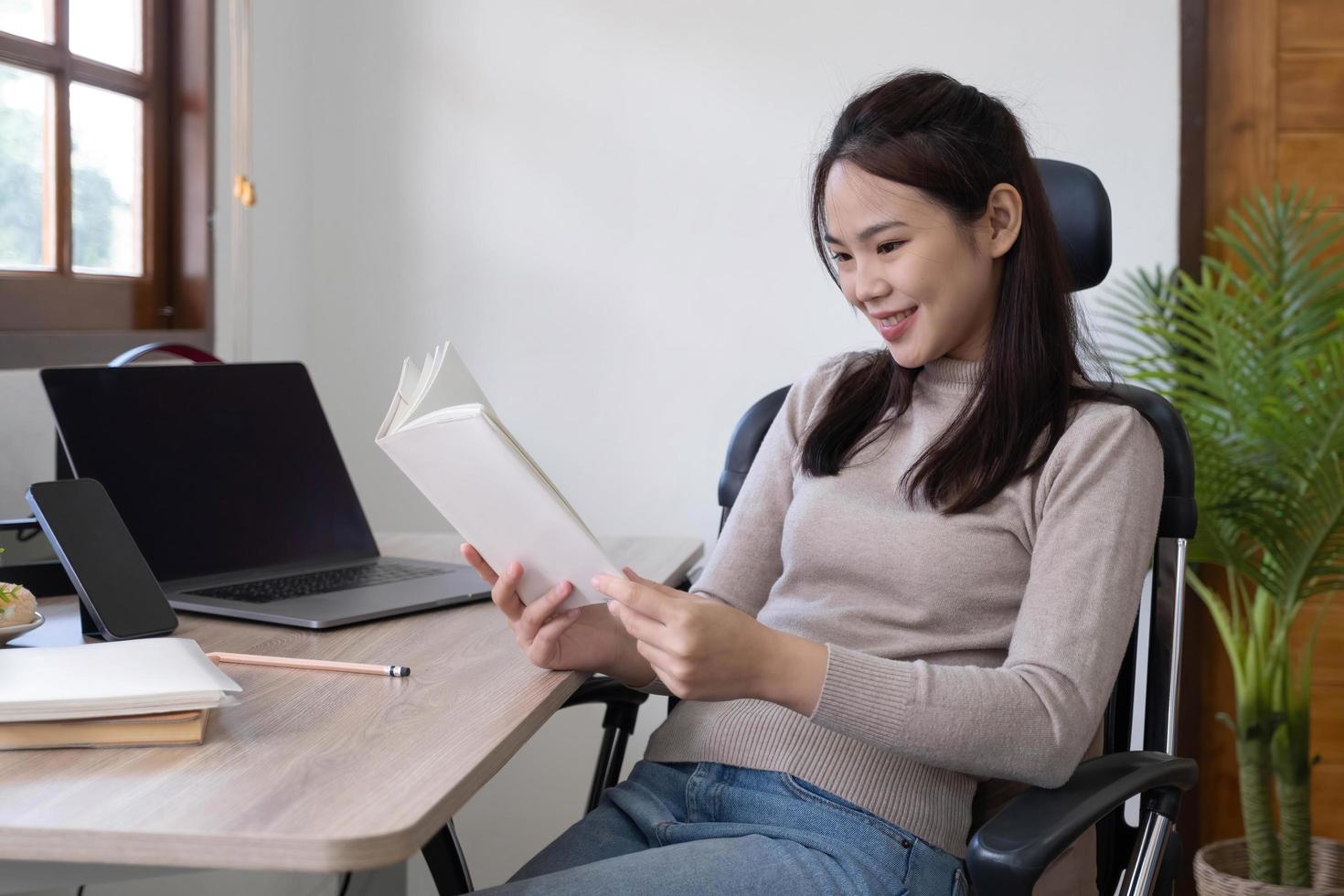 Smiling Asian woman reading book while sitting at home photo