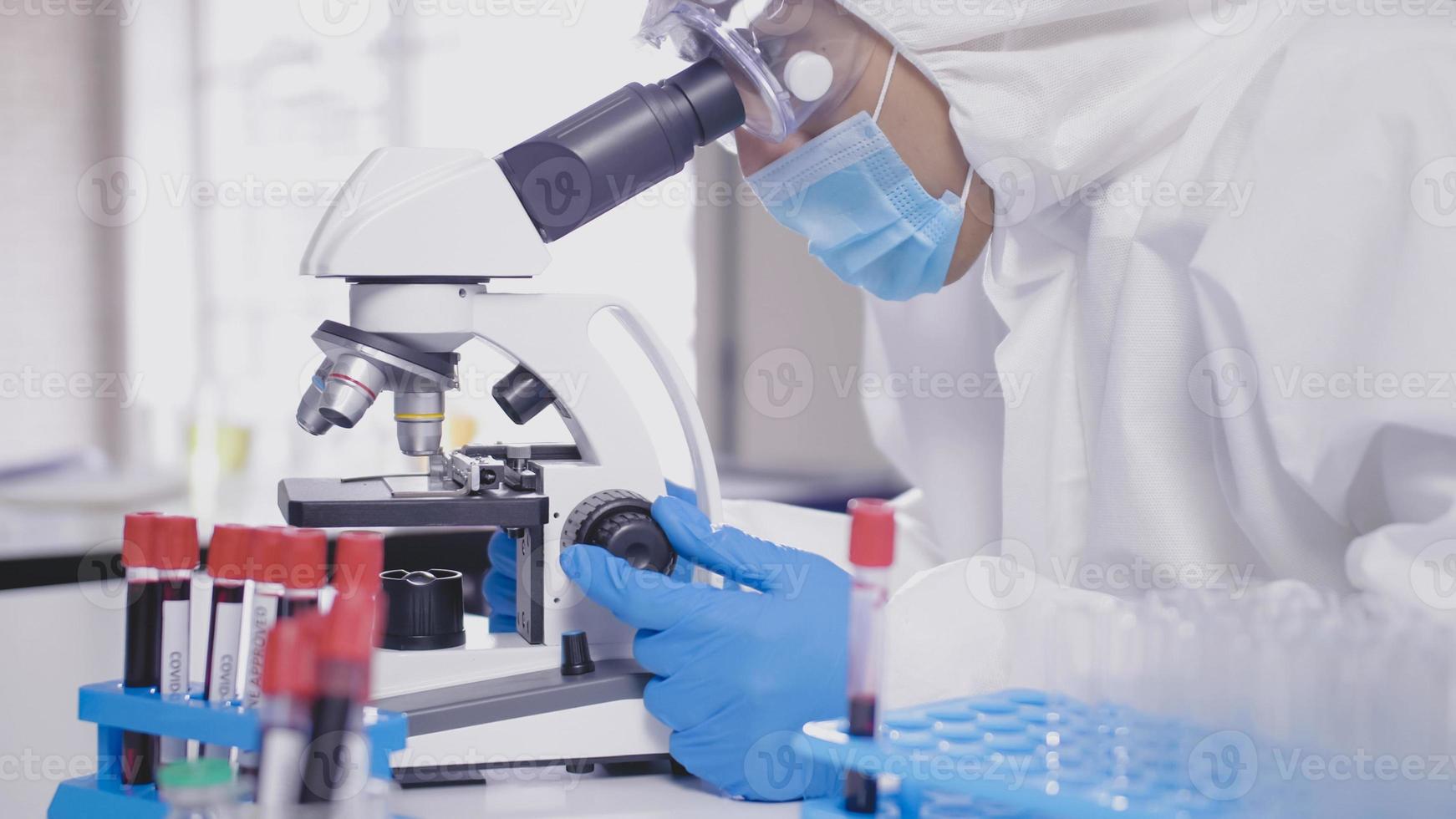 Scientist in PPE suite doing some research and looking through a microscope in laboratory photo
