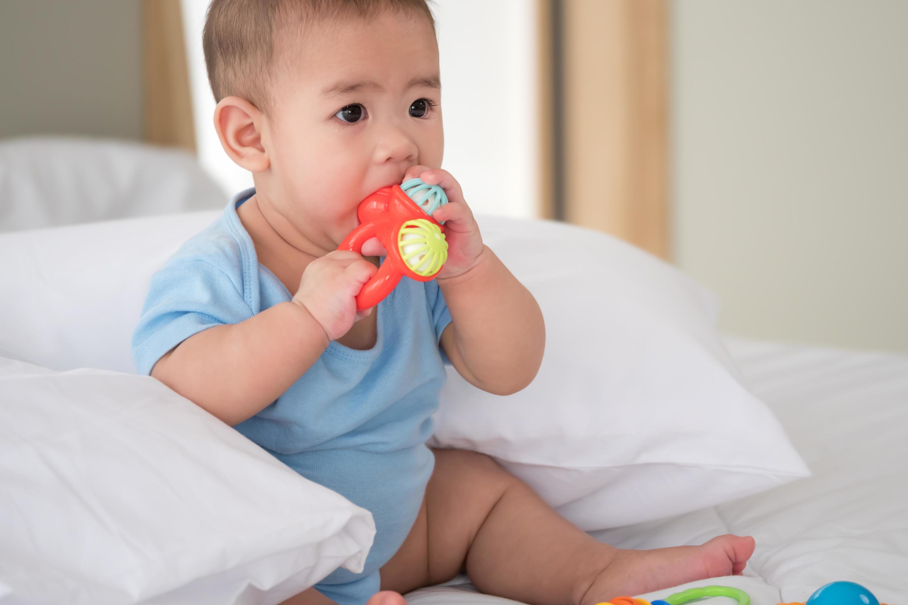 Un lindo bebé recién nacido con ropa ligera está jugando con juguetes  educativos tirados en el suelo sobre una manta de lino gris. vista  superior. productos para niños. feliz infancia y maternidad.