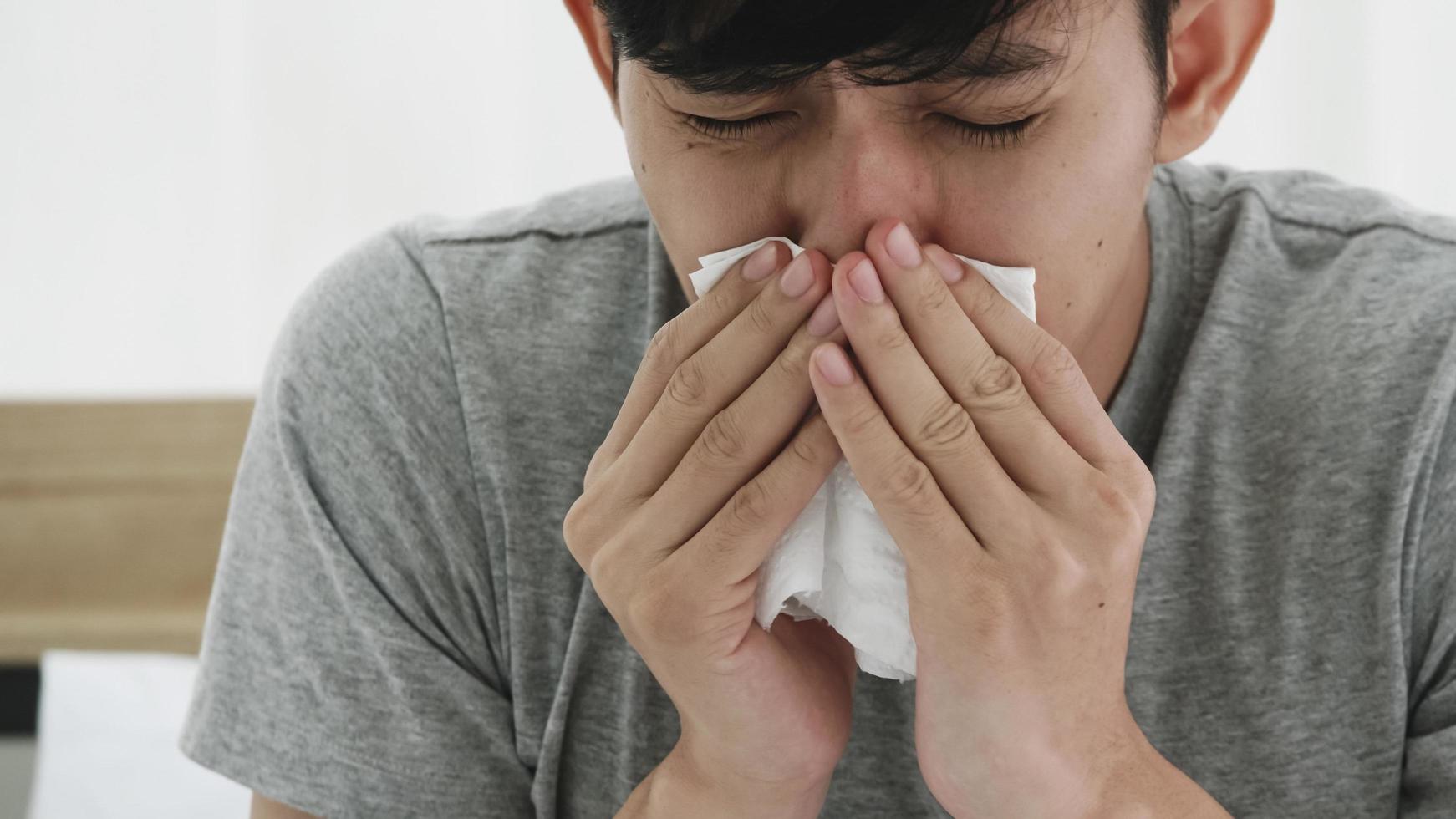 Young man blowing nose while lying sick in bed at home photo