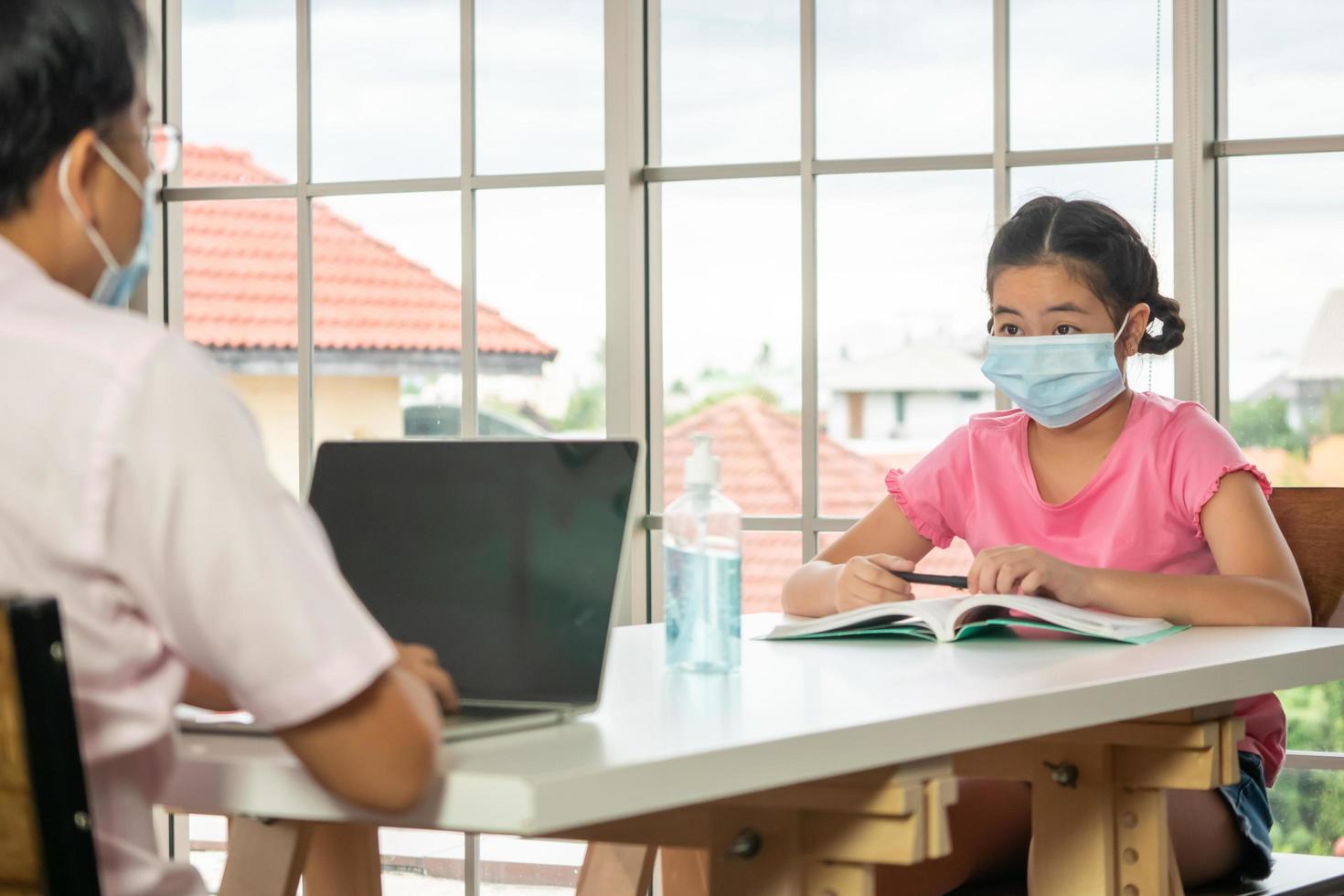 Father and daughter wear protective masks and keep the social distance while working at home. photo