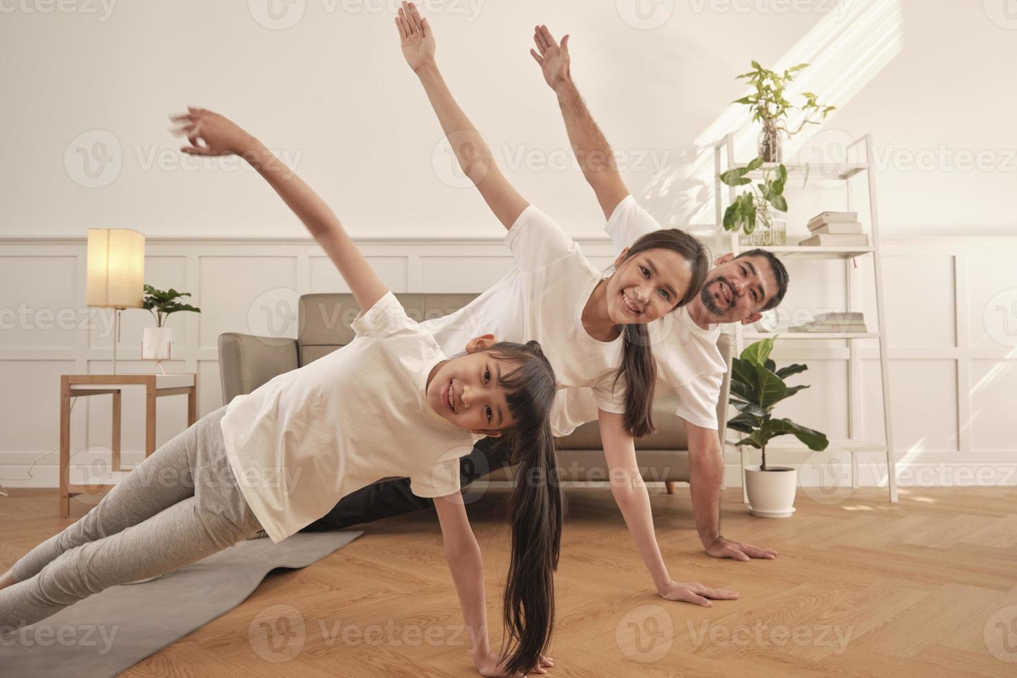 Asian Thai parents and daughter fitness training exercise and practice yoga on living room floor, lovely rowing together for health and wellness, and happy domestic home lifestyle on family weekend. photo