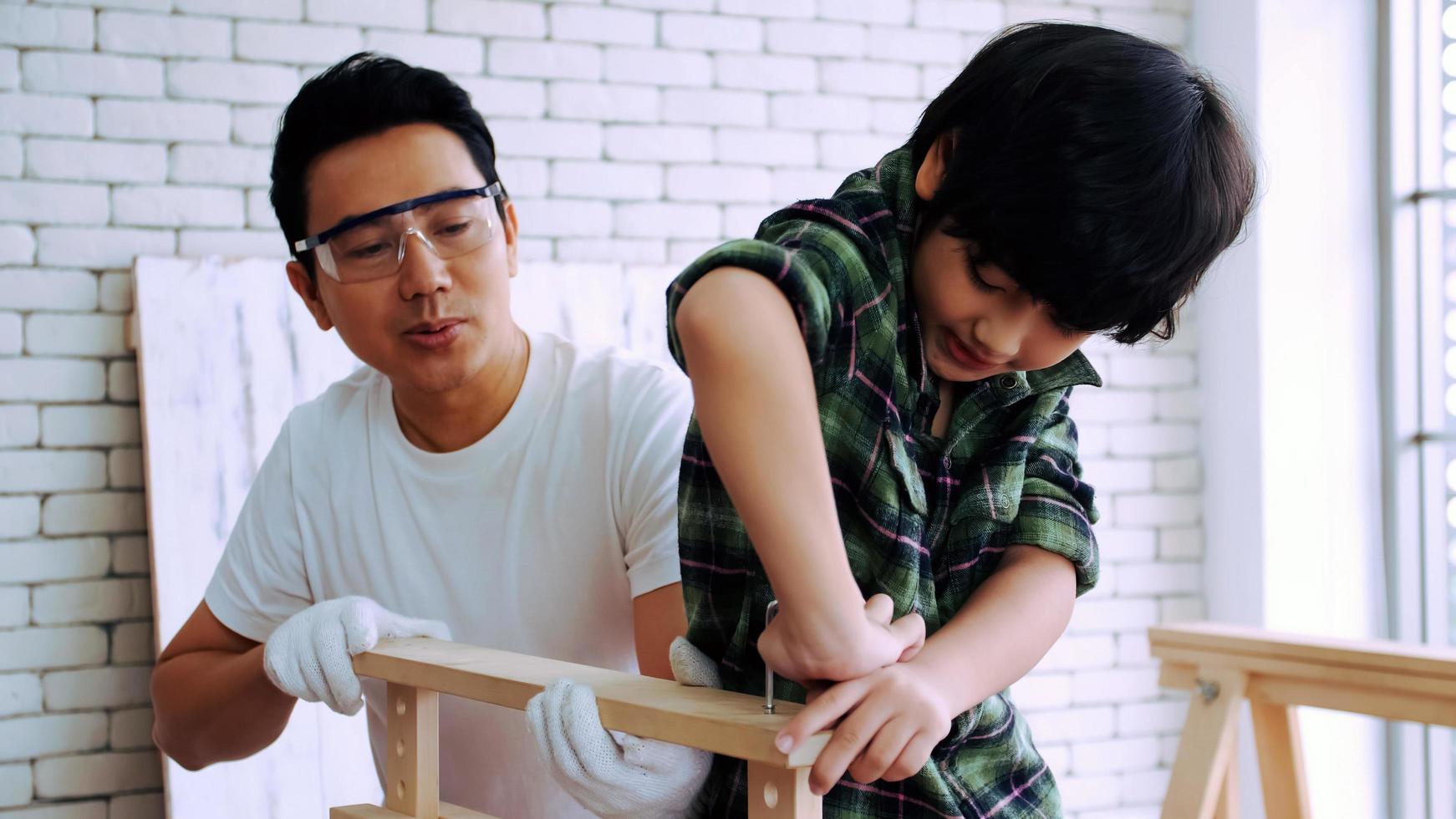 joven carpintero enseñando a su hijo a trabajar con madera en el taller. foto