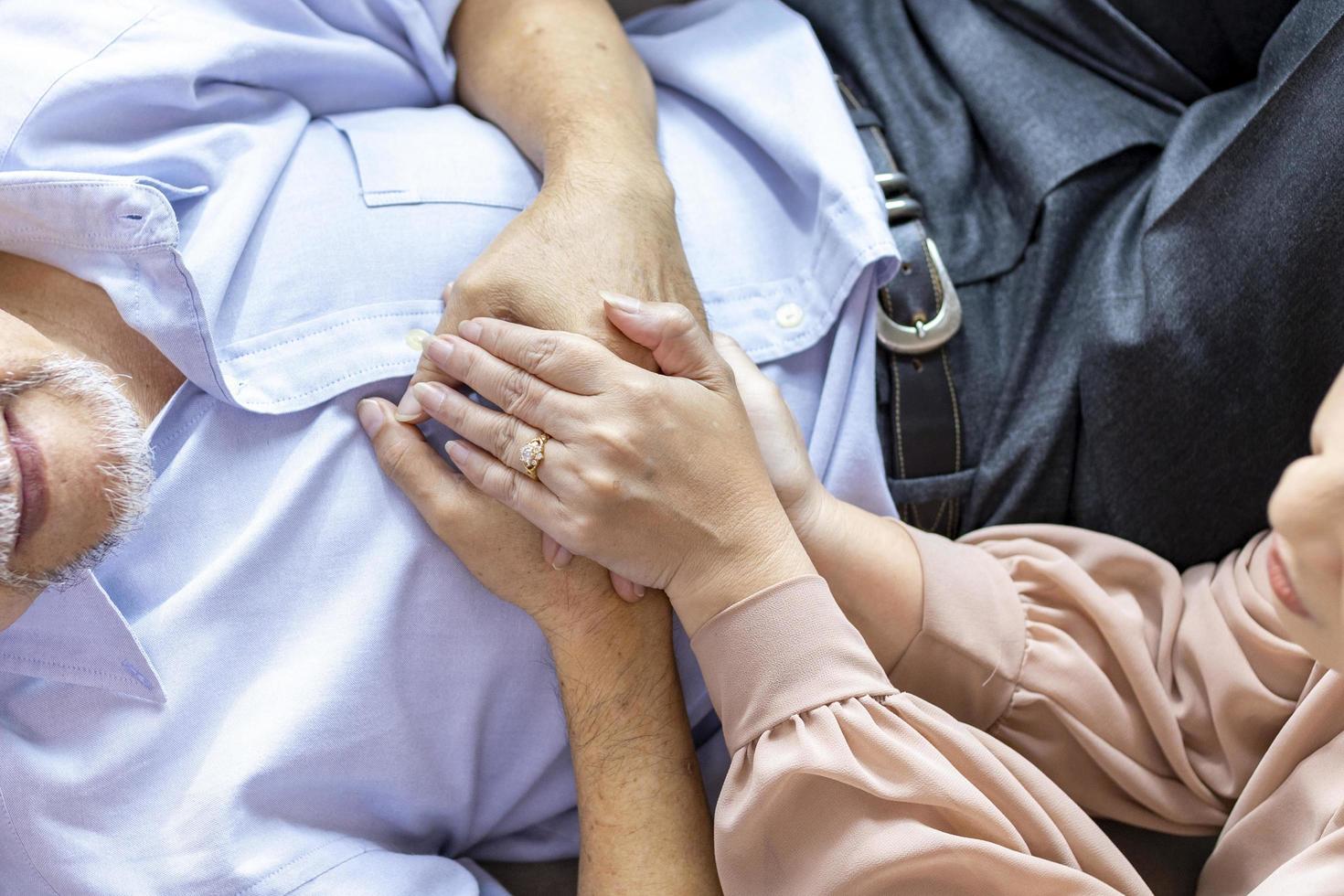 Senior man is suffering from heart attack while his wife is holding his hand for sympathy support and encouragement for compassion and condolence concept photo