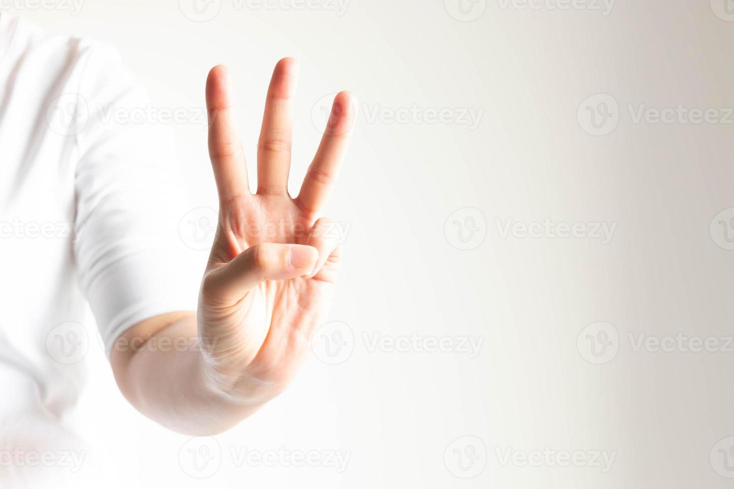 A hand showing number three by raising forefinger, middle finger and ring finger in close-up on white background and little light. photo