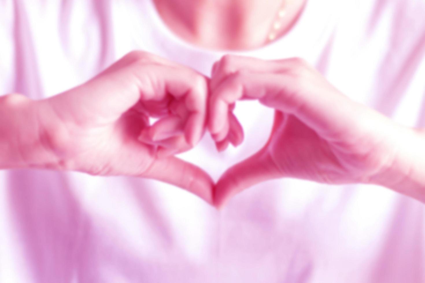 Blurry image of hand signs to be heart shape, showing love in pink color tone photo. photo