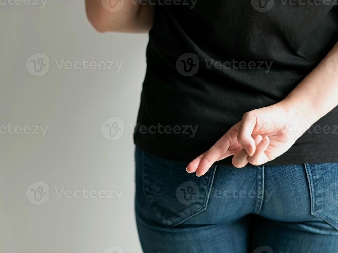 A woman hide a hand signals, forefinger and middle finger crossing together, behind her back when saying a lie. photo