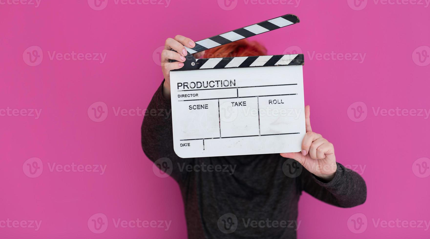 redhead woman holding movie  clapper on pink background photo