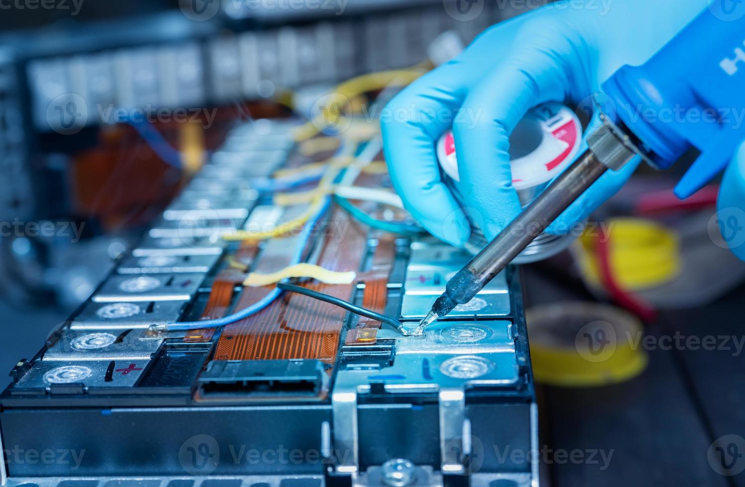 Technician use soldering iron to solder metal and wire of lithium-ion rechargeable battery. Repair module of Li-ion battery. Engineer hand holds soldering iron and tin-lead to solder electronic board. photo