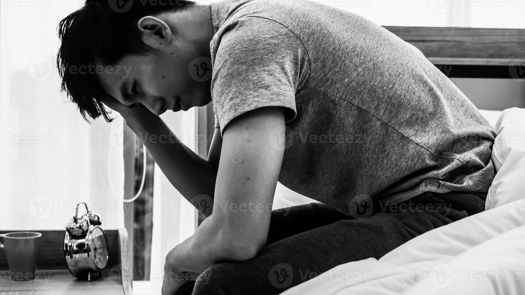 Stressed Asian young man sitting alone on bed. Bad relationship or bankrupt problem and sickness concept. photo