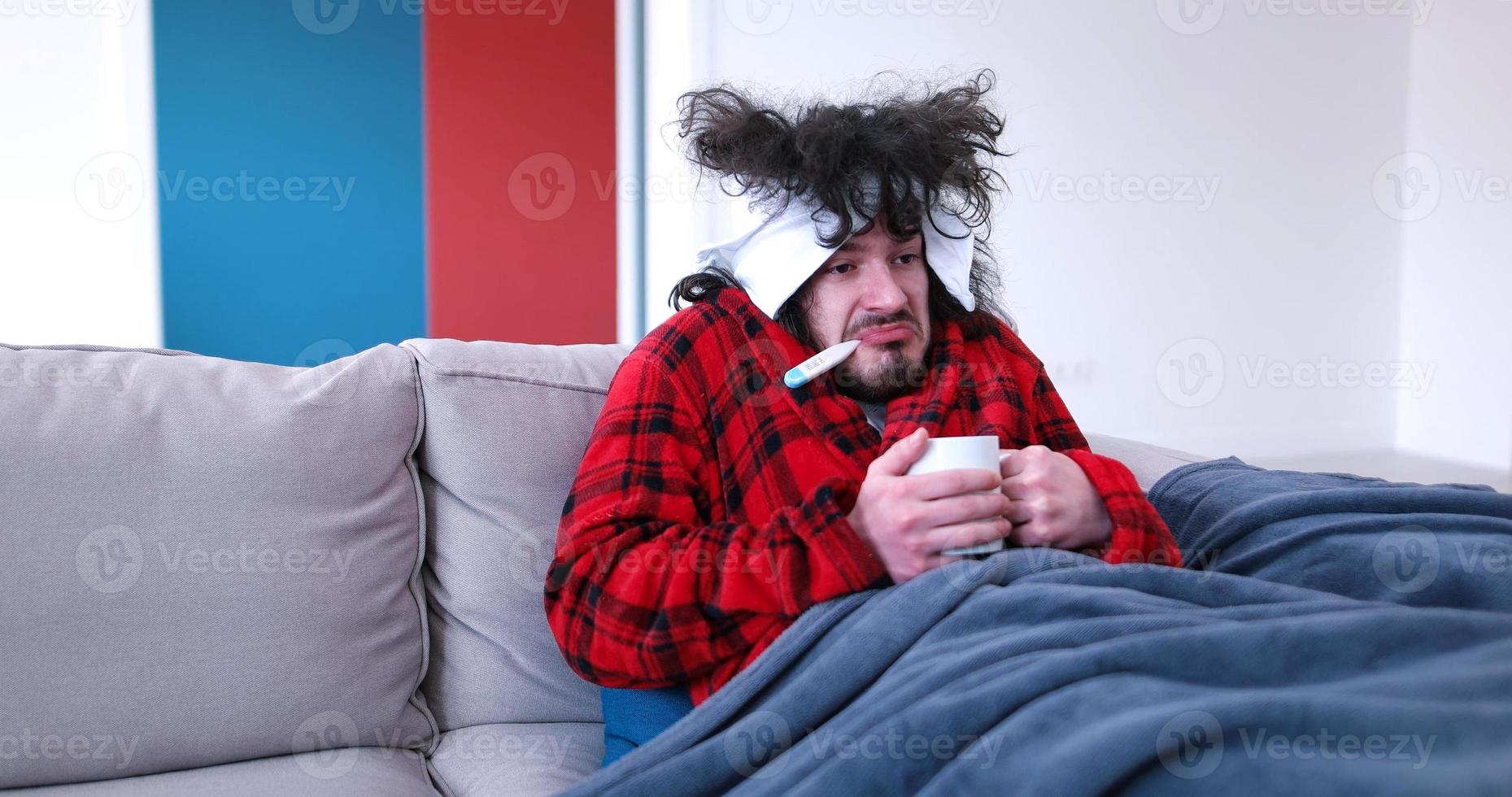 sick man is holding a cup while sitting on couch photo
