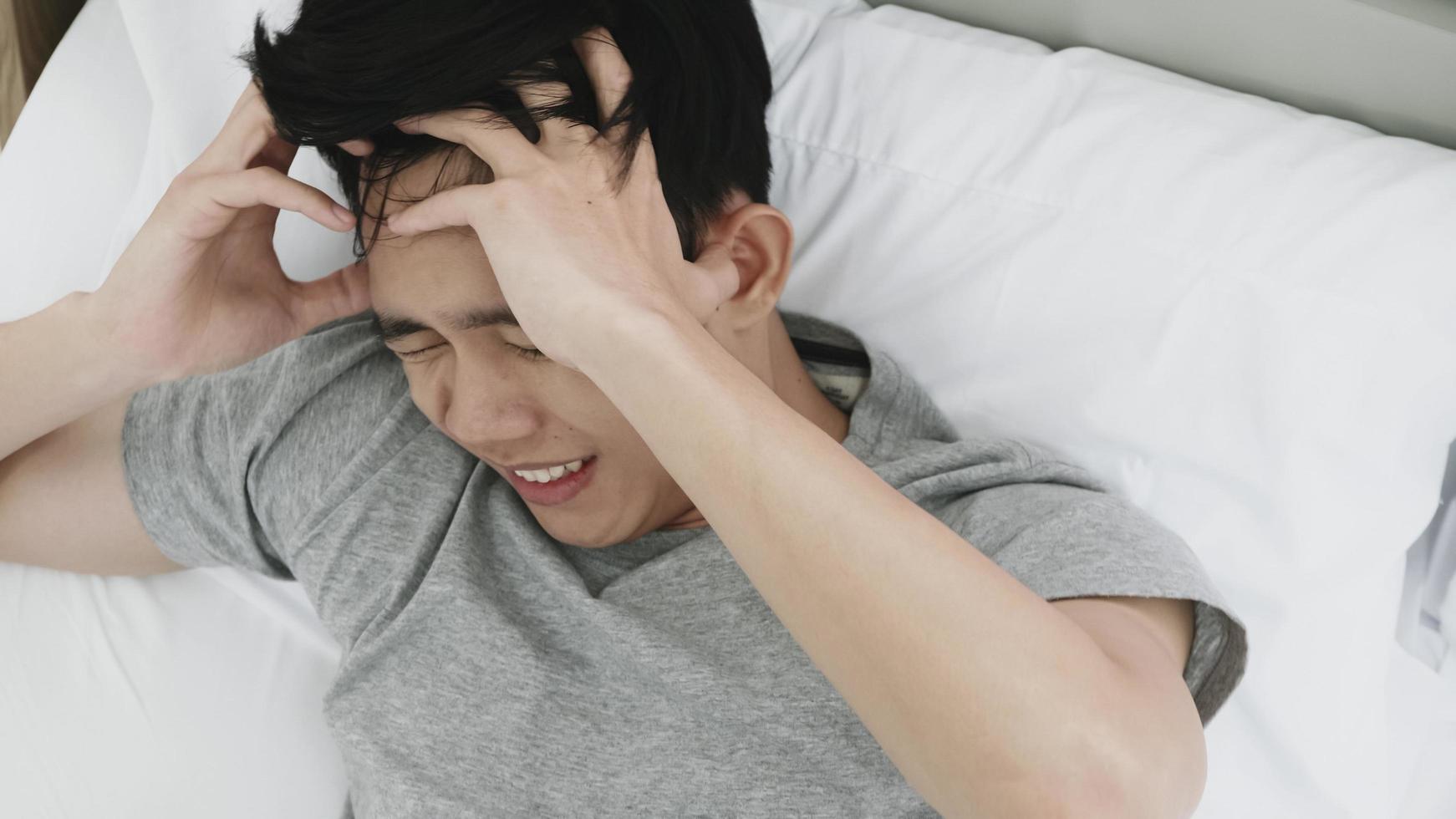 Young man suffering from headache lying on bed at home photo