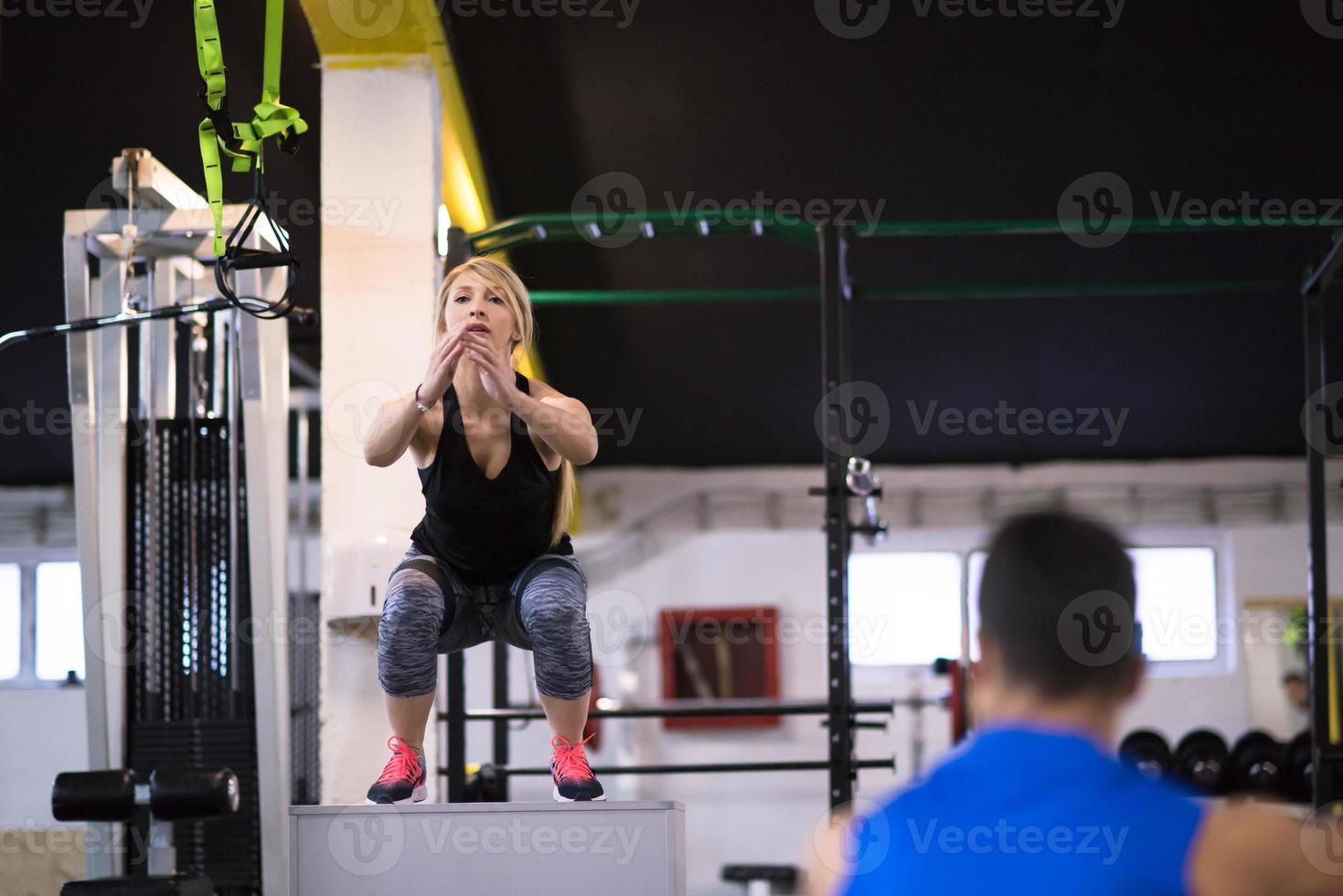 woman working out with personal trainer jumping on fit box photo