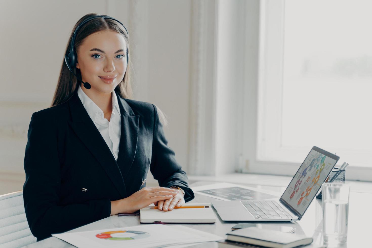 Happy business lady in headset analyzing graphs charts photo