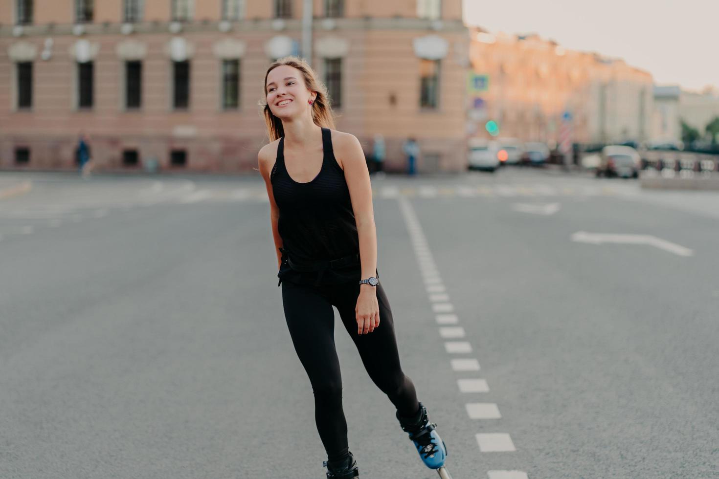 Healthy lifestyle summer leisure active outdoor recreation concept. Smiling dark haired young woman enjoys rollerblading as hobby looks into distance wears sportsclothes rides fast on rollers photo