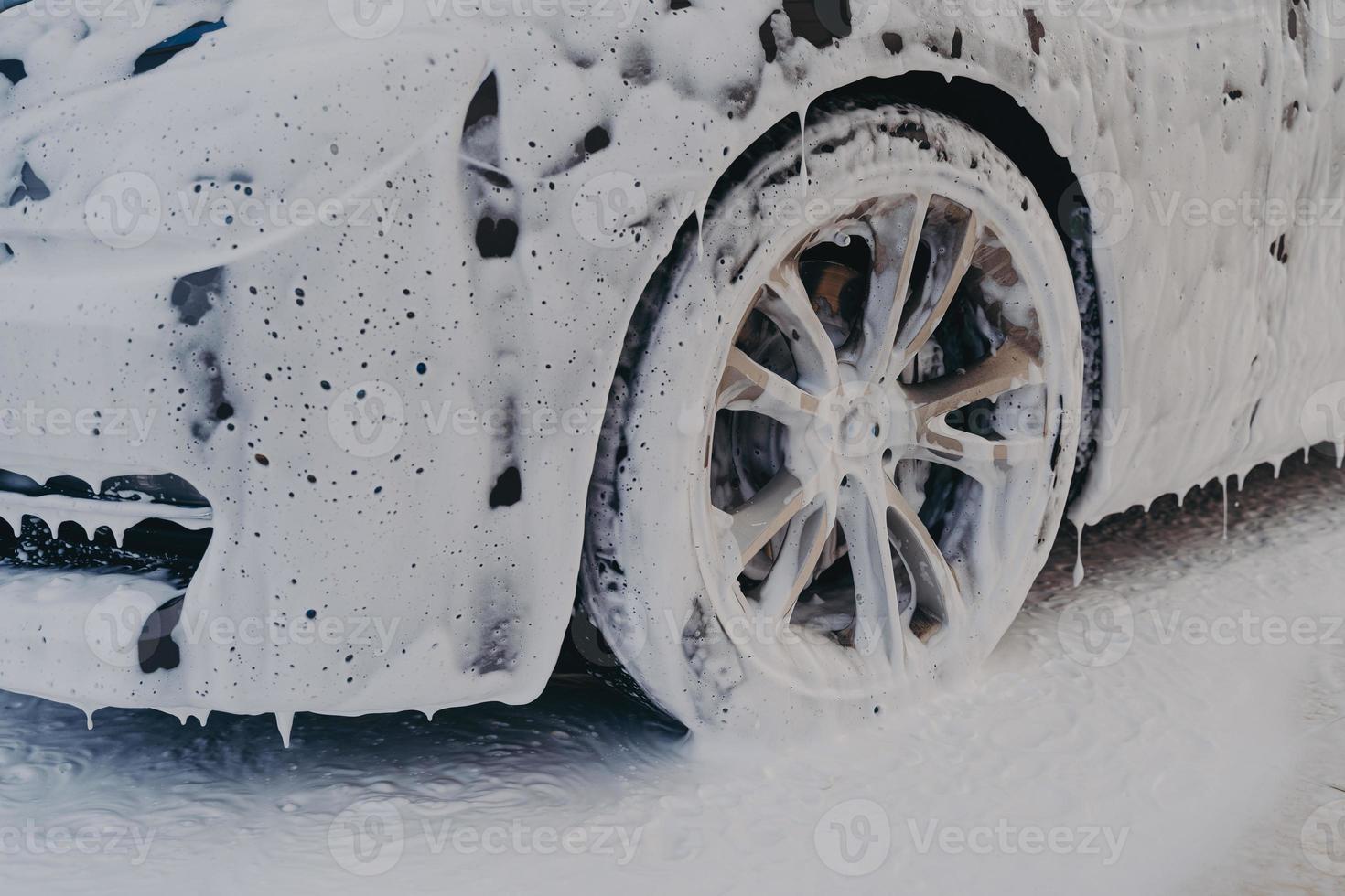 Car wheel in white soap foam at carwashing service station photo