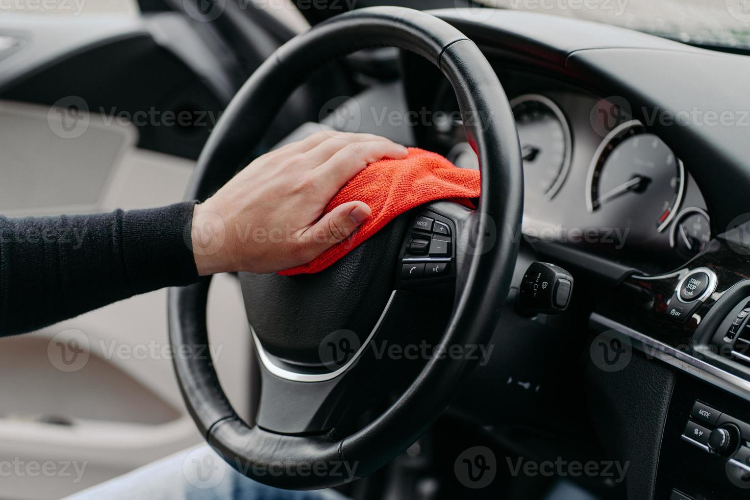 Close up shot of mans hand cleaning car steering wheel with microfiber cloth. Hygiene prevention during coronavirus outbreak photo