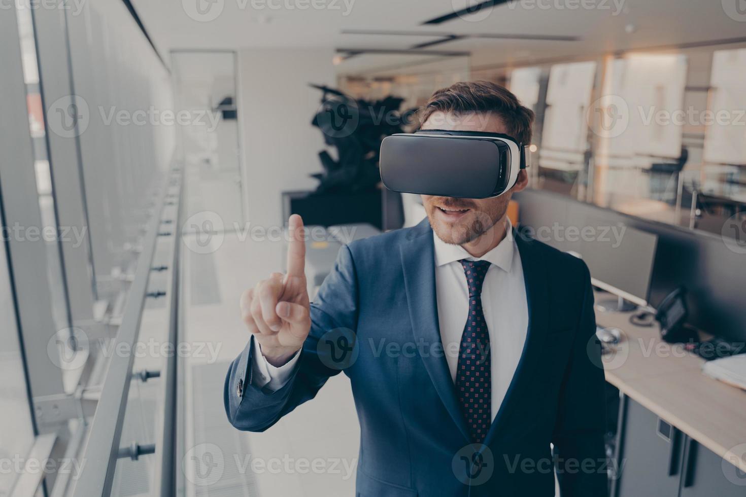 Young businessman in elegant suit using VR headset, touching exploring virtual reality at work photo