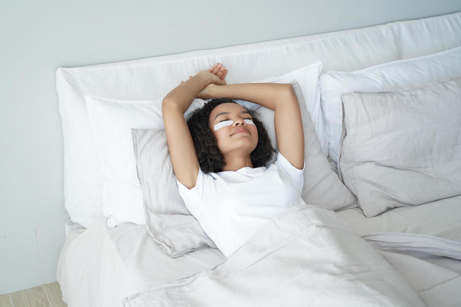 chica afro feliz duerme con parches en los ojos. mujer joven relajándose en casa en la mañana del fin de semana en la cama. foto