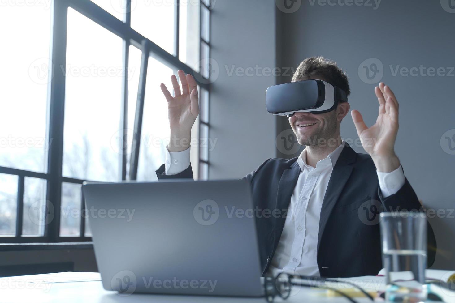 Young businessman in suit sitting at office table and using vr glasses goggles at work photo