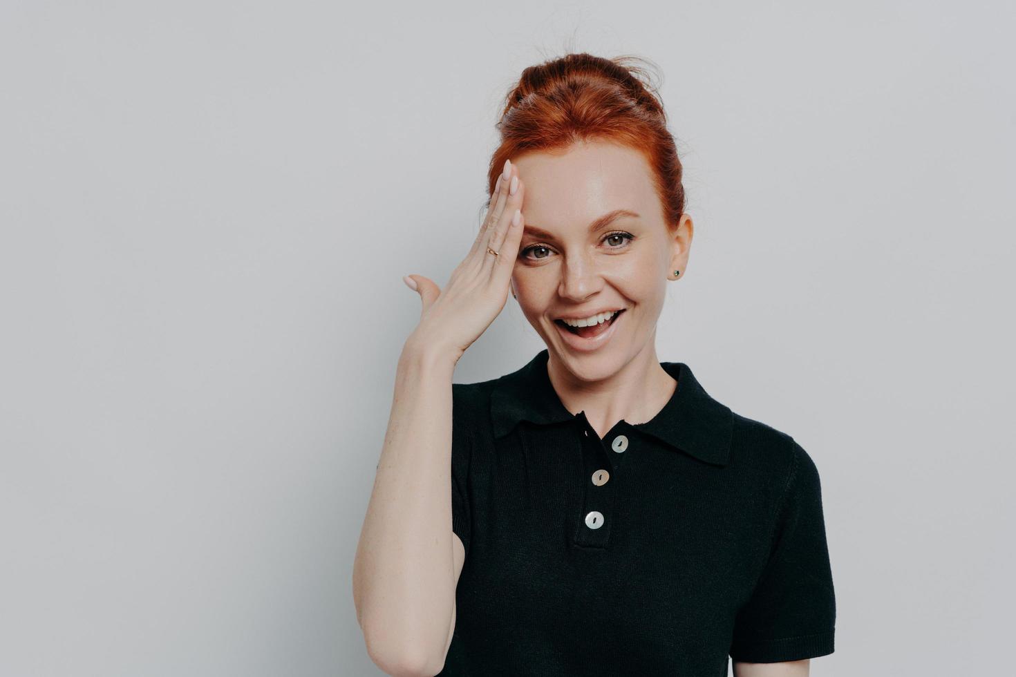 Pretty red-haired woman with hair in bun forgetting something, isolated on grey background photo