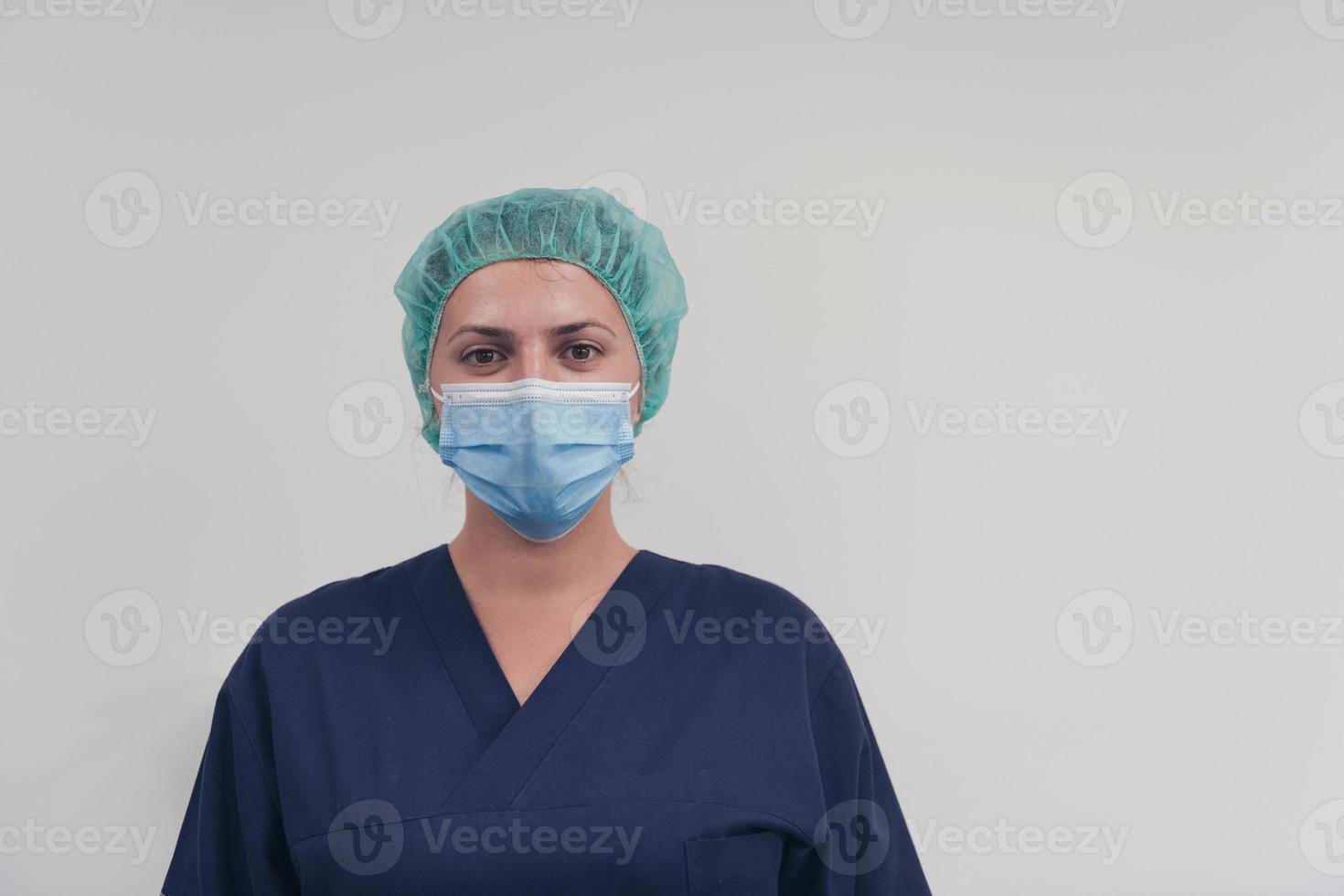 Close up of female doctor or scientist with a medical mask and surgical cap over grey background. She is adjusting mask with photo