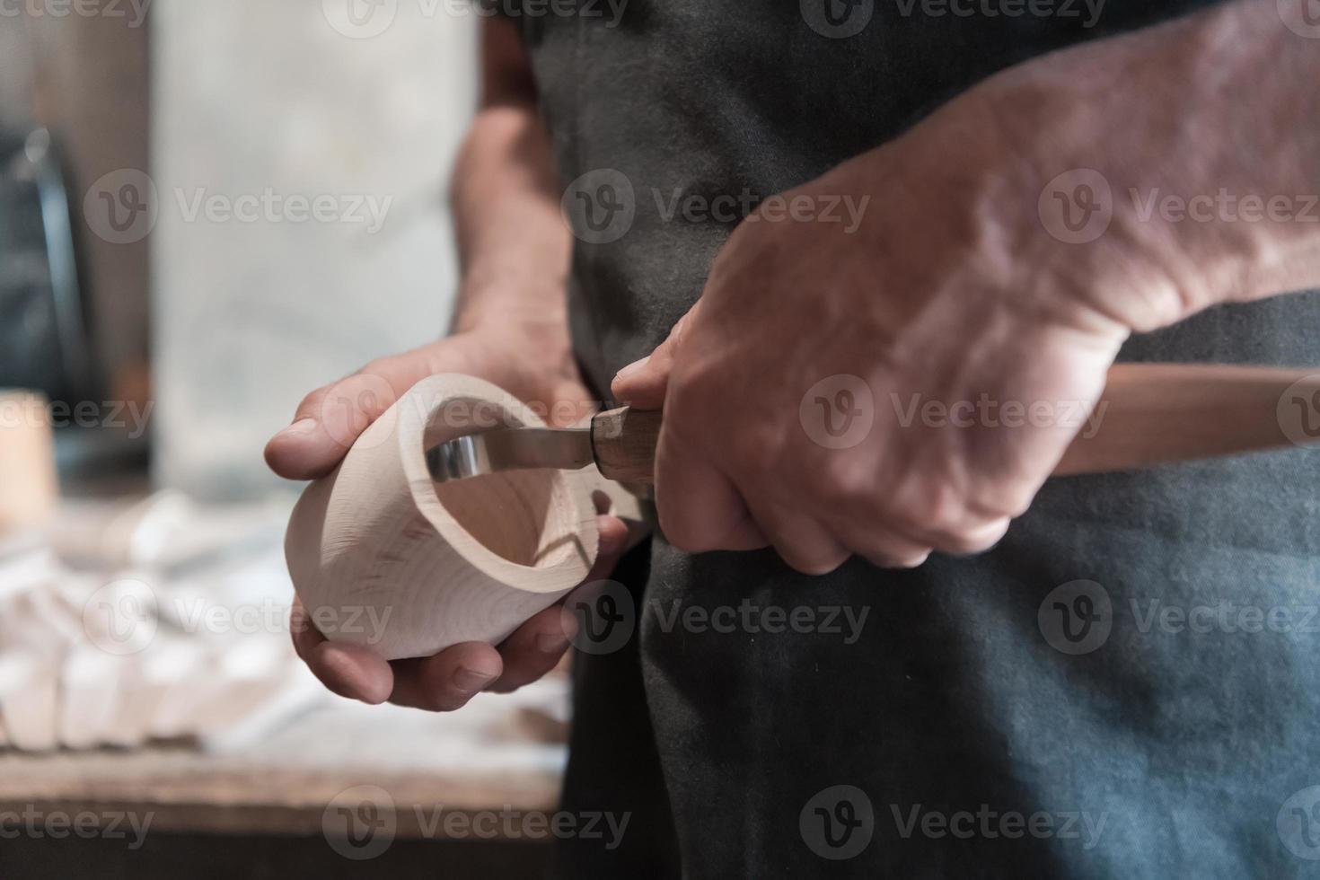 Hands carving cup from wood, working with chisel close up. Wooden workshop. Process of making wooden kitchenware photo