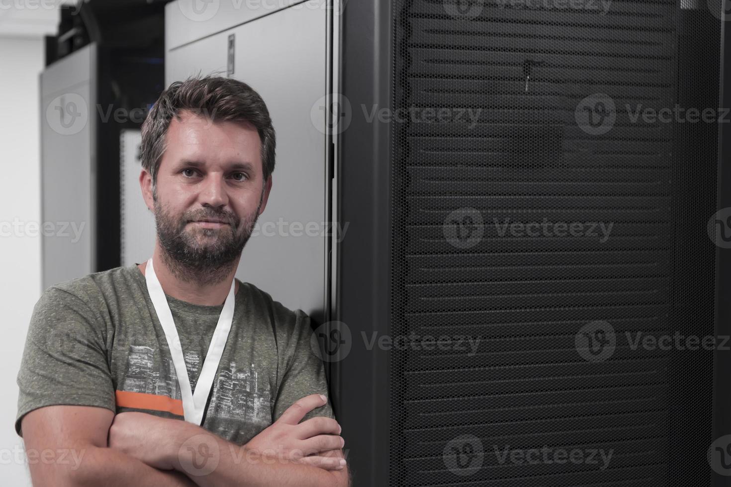 Portrait of male technician or network administrator standing brave as a hero with arms crossed in data center server room. photo