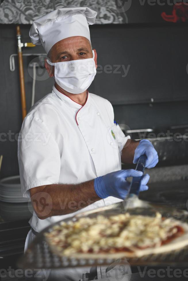 chef con mascarilla protectora de coronavirus preparando pizza foto